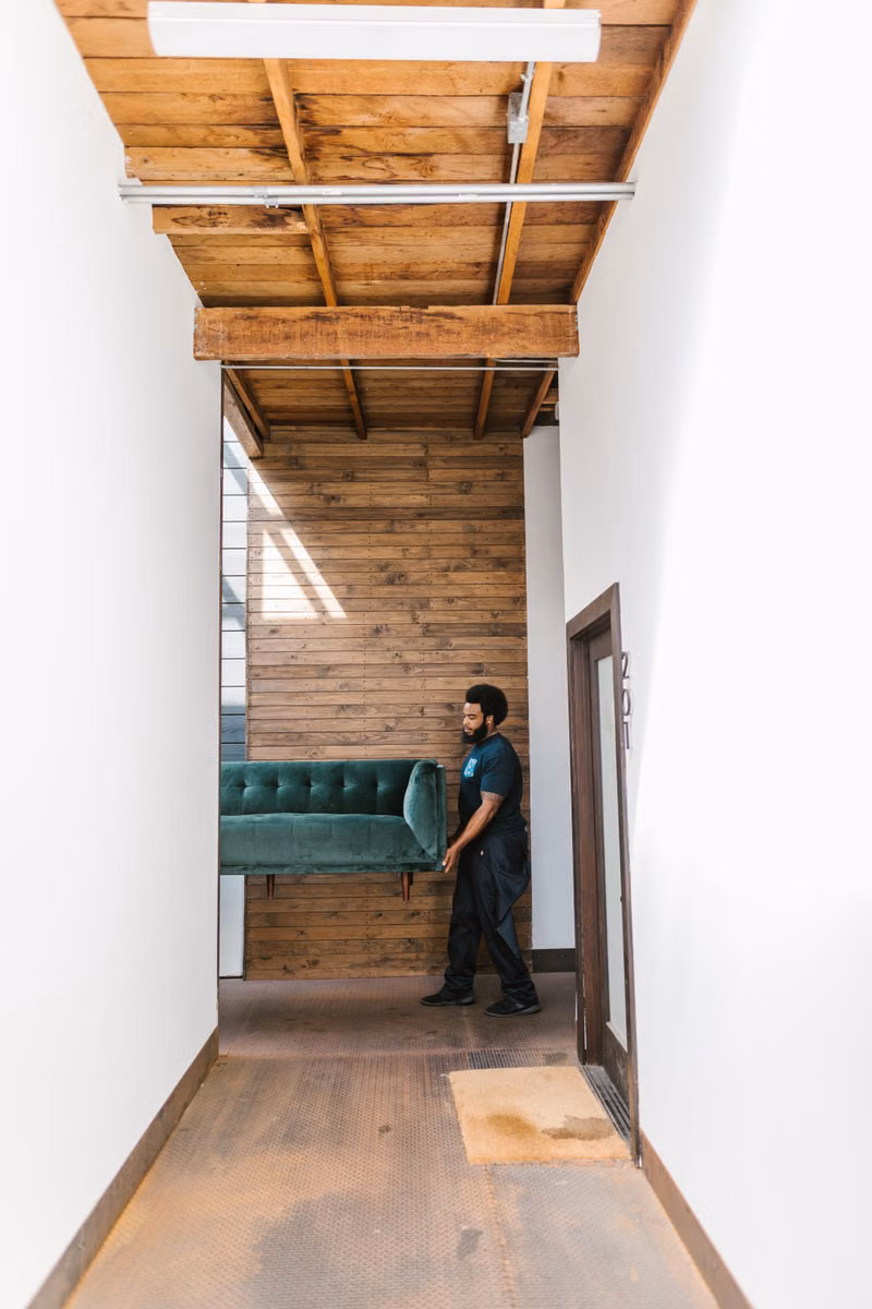 Junk removal workers carefully carrying an old couch through a residential doorway